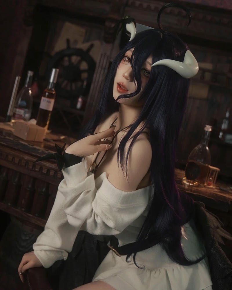 Albedo cosplay ngồi bên bàn gỗ trong phòng tối
