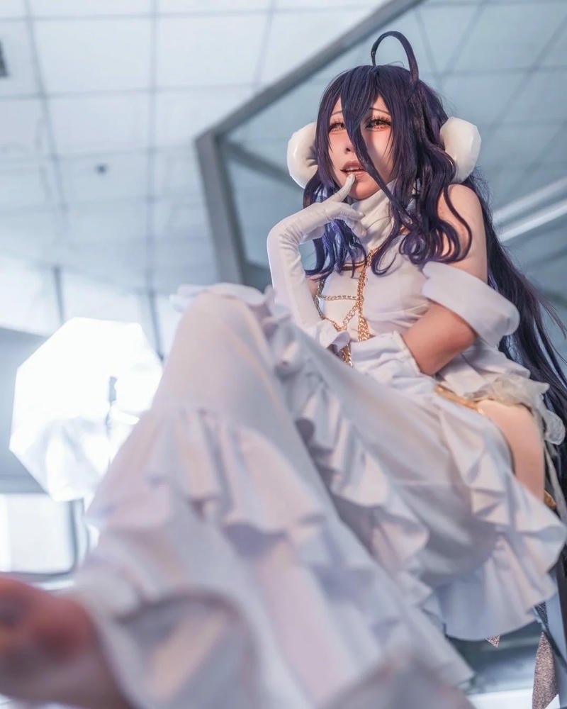 Albedo cosplay váy trắng nằm trên sàn nhà lót thảm